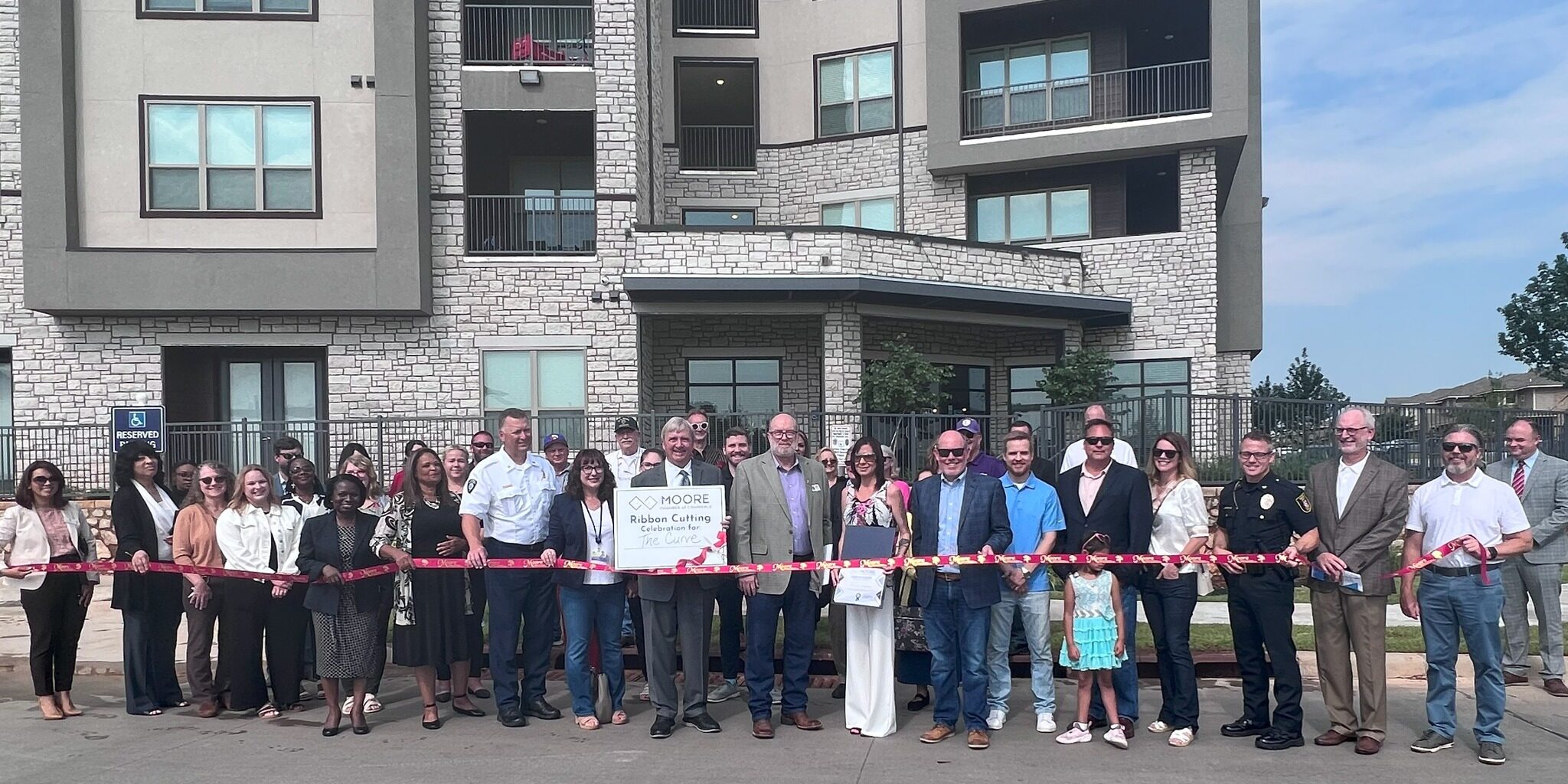 People cutting a ribbon in front of The Curve Apartments